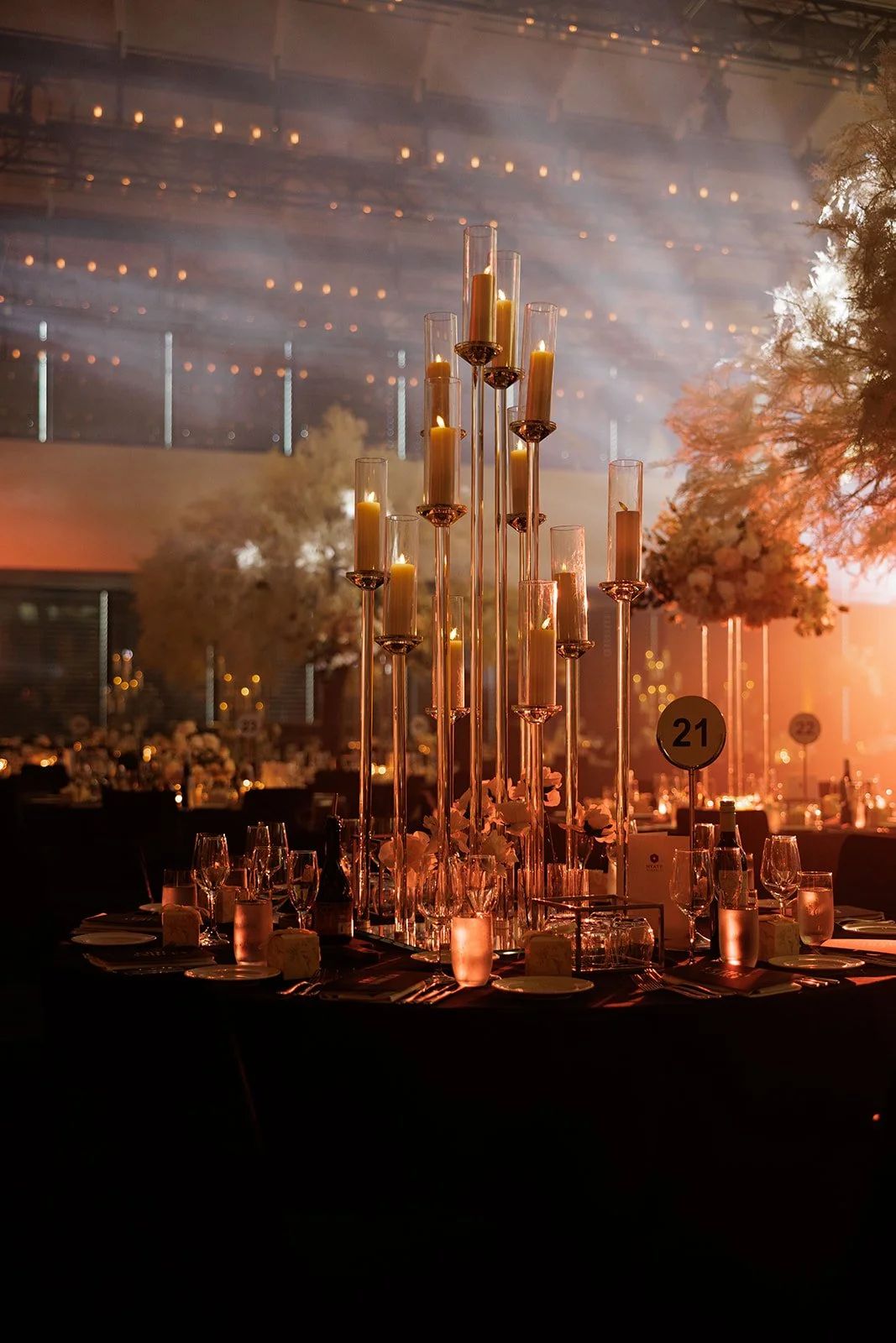 Elegant banquet table with tall candle centerpieces and floral arrangements in a dimly lit, spacious event venue.