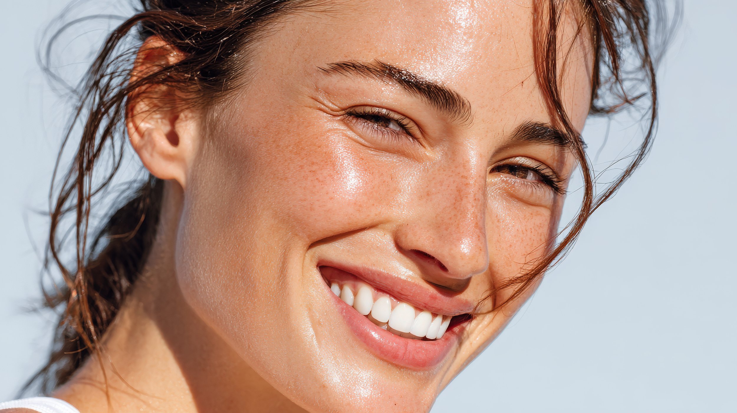 A close-up of a smiling woman with wet, wavy hair and sun-kissed skin.