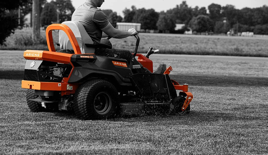 Person operating a robotic lawn mower on a grassy field.