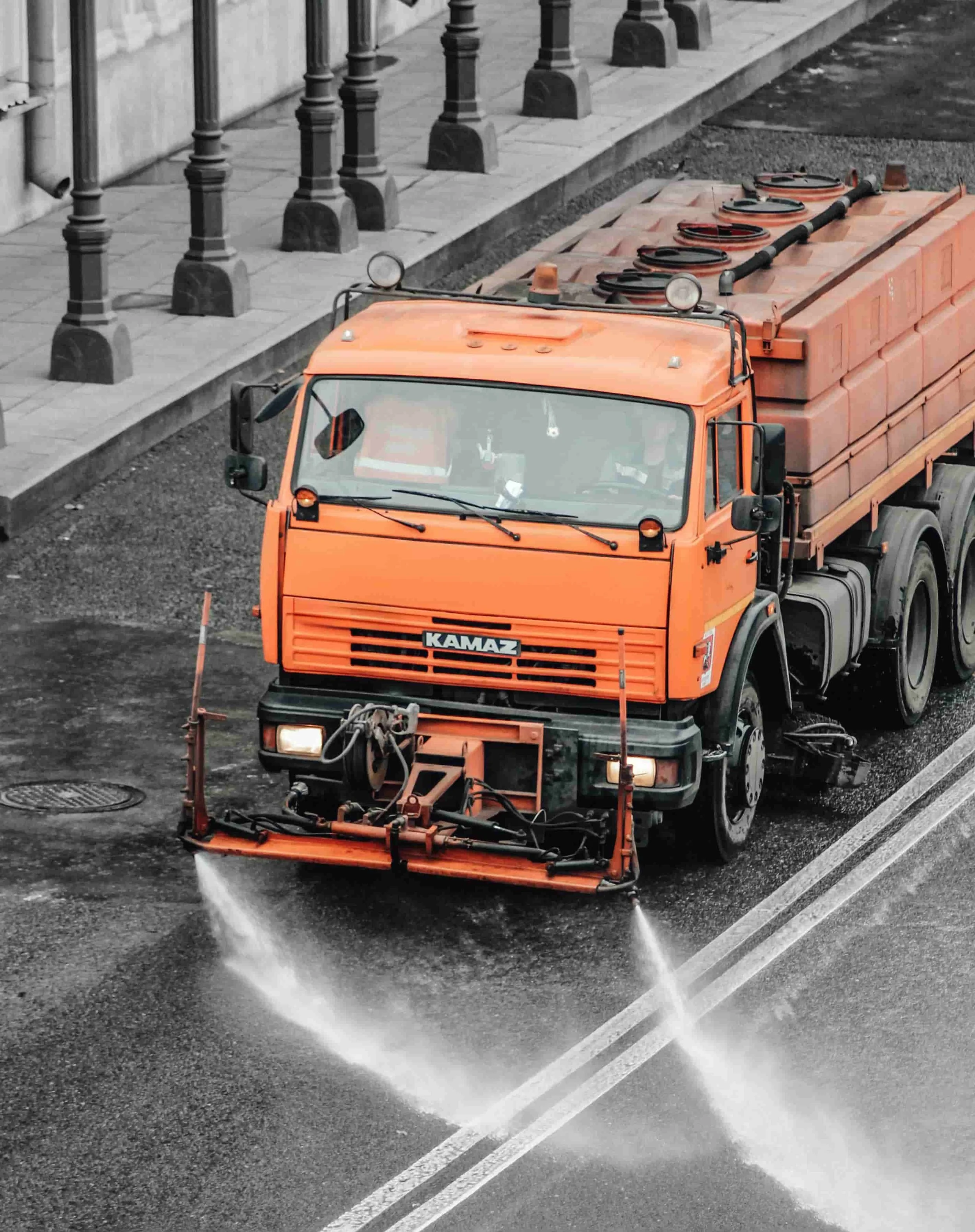 An orange street cleaning vehicle spraying water on a paved road surface.