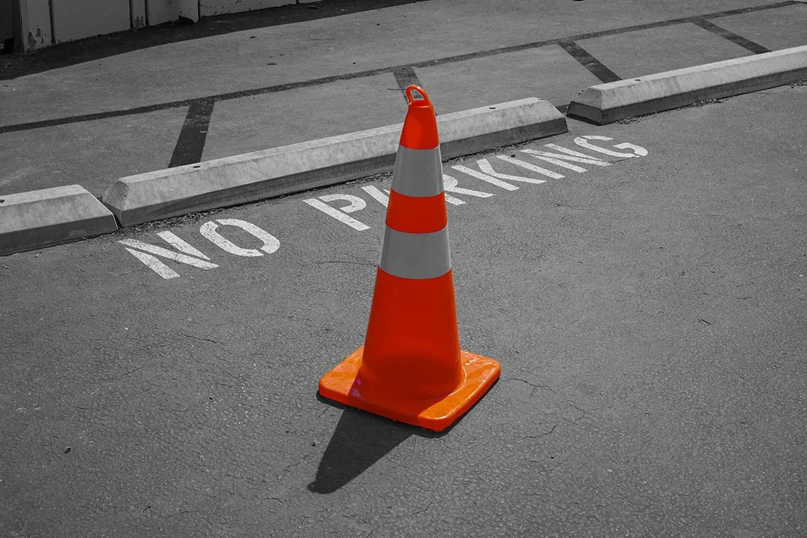A traffic cone placed in front of a no parking zone in a parking lot.