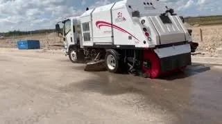 A street sweeper vehicle cleaning a road surface outdoors during daytime.