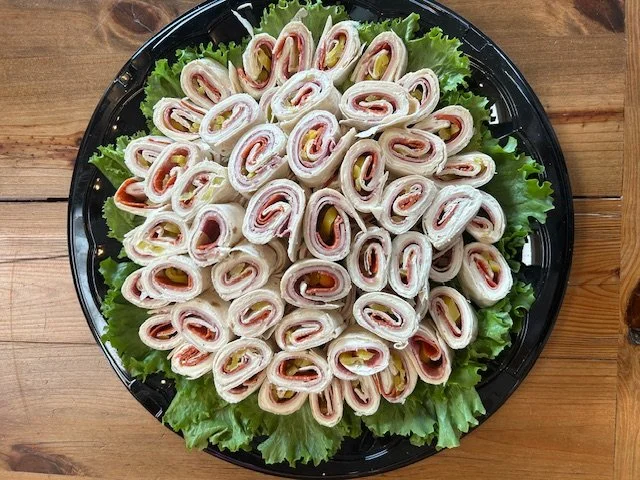 Plate of rolled ham and cheese sandwiches on a bed of lettuce, arranged in a circular pattern.