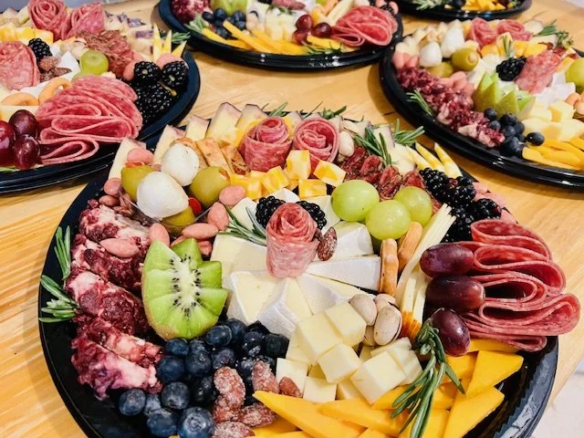 Assorted cheese, fresh fruits like kiwi, grapes, blackberries, and blueberries, assorted sliced meats, and garnishes arranged on black platters for a party or gathering.