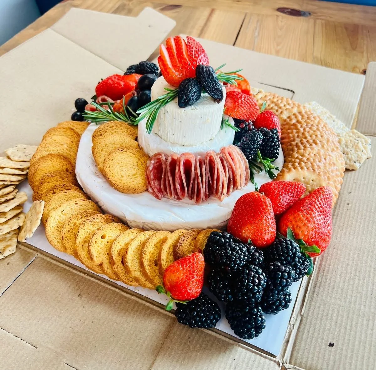Cheese board with strawberries, blackberries, grapes, crackers, and a wheel of brie cheese topped with strawberries, blackberries, grapes, and rosemary.