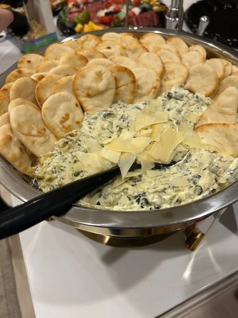 A chafing dish filled with crackers and a cheese spread topped with shredded cheese.
