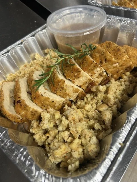 Fried chicken strips with a sprig of rosemary, served with crumbled fried chicken pieces and a side of dipping sauce in a plastic container.