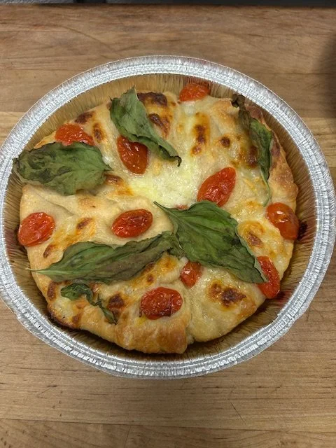 Individual serving of Margherita pizza with cheese, cherry tomatoes, and basil leaves in a foil container.