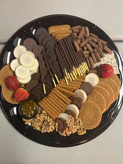 Assorted cookies, strawberries, chocolate-covered pretzels, and nuts on a black platter.