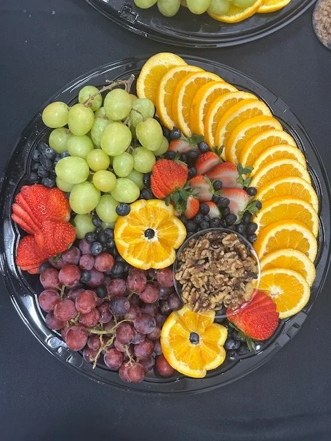 Assorted fresh fruit platter with green grapes, sliced oranges, strawberries, red grapes, blueberries, and a small container of mixed nuts.