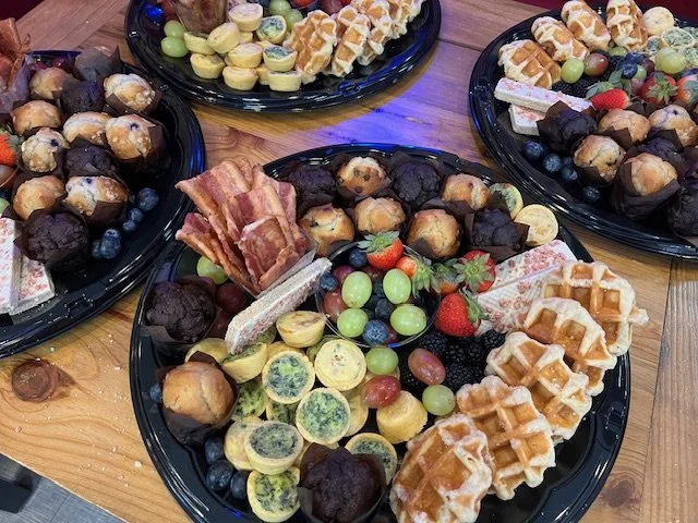 Platters of assorted mini desserts, including waffle cones, cookies, strawberries, grapes, blueberries, and various pastries, arranged on a wooden table.