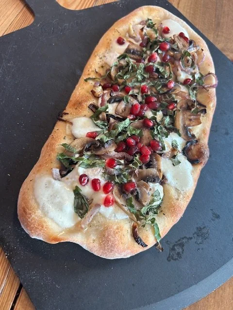 Flatbread pizza topped with cheese, mushrooms, chopped herbs, pomegranate seeds, and a drizzle of balsamic glaze
