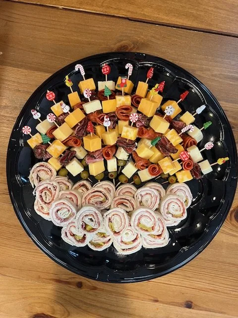 Charcuterie platter with cheese, meats, and rolled sandwiches on a black tray.
