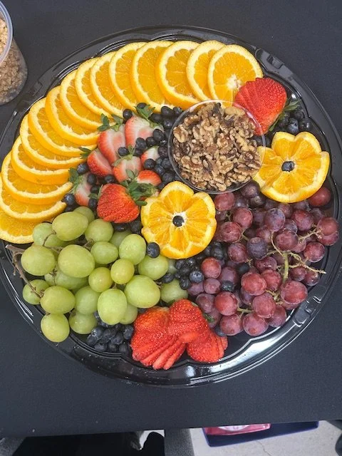 An assorted fruit platter with orange slices, green and red grapes, strawberries, blueberries, and orange slices with a bowl of chopped walnuts in the center.