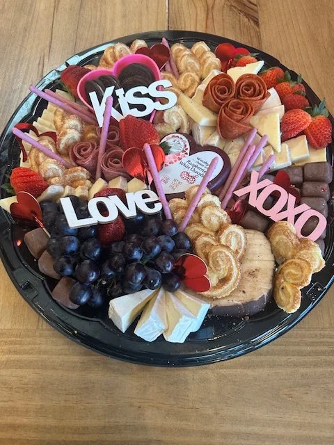 Charcuterie board with grapes, strawberries, cheese, cookies, and decorative love-themed signs.