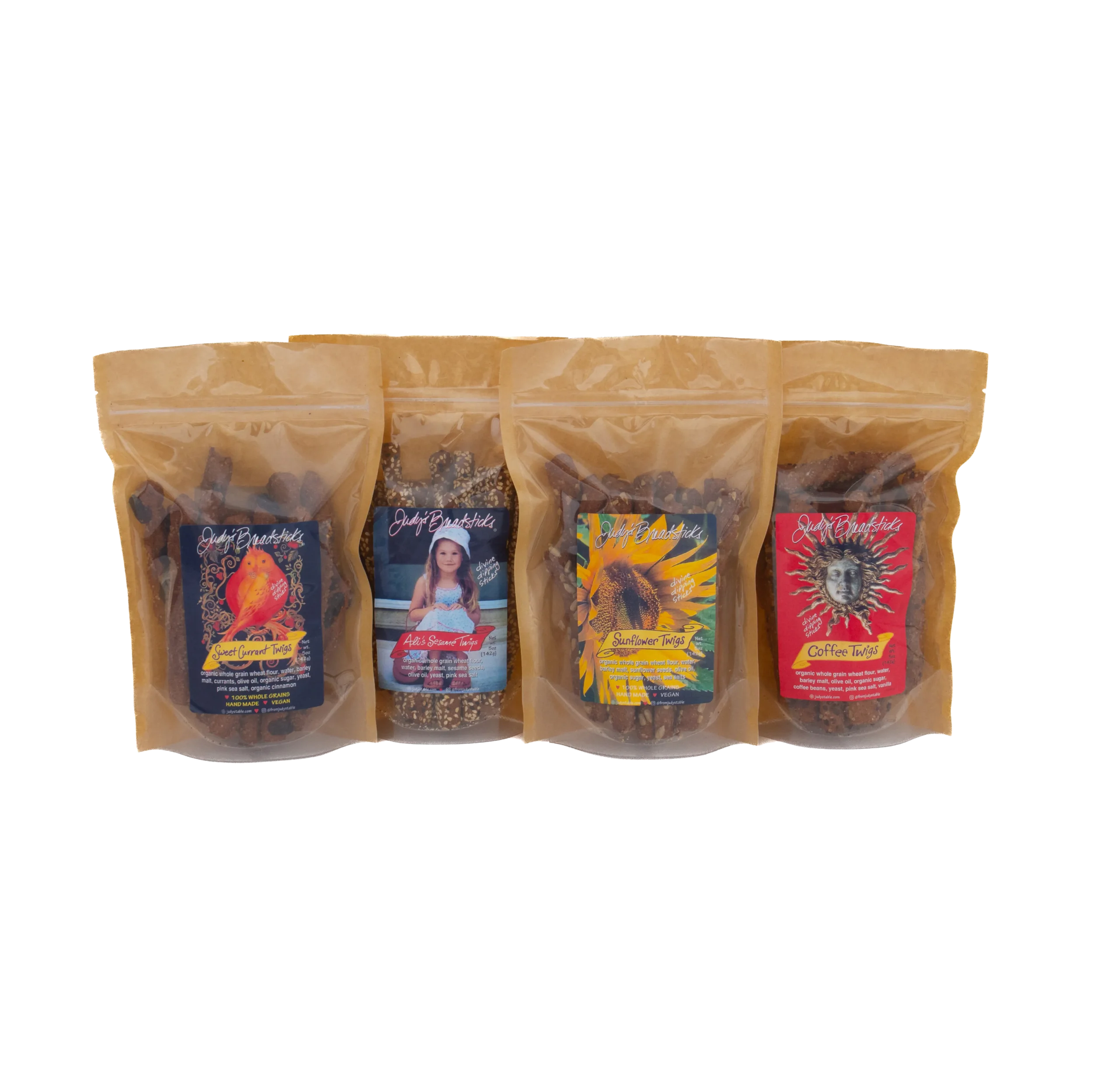 Four transparent plastic bags with colorful labels containing different varieties of organic Judy's Table twigs such as sweet currant, sesames, sunflower, and coffee, arranged in a row against a plain white background.
