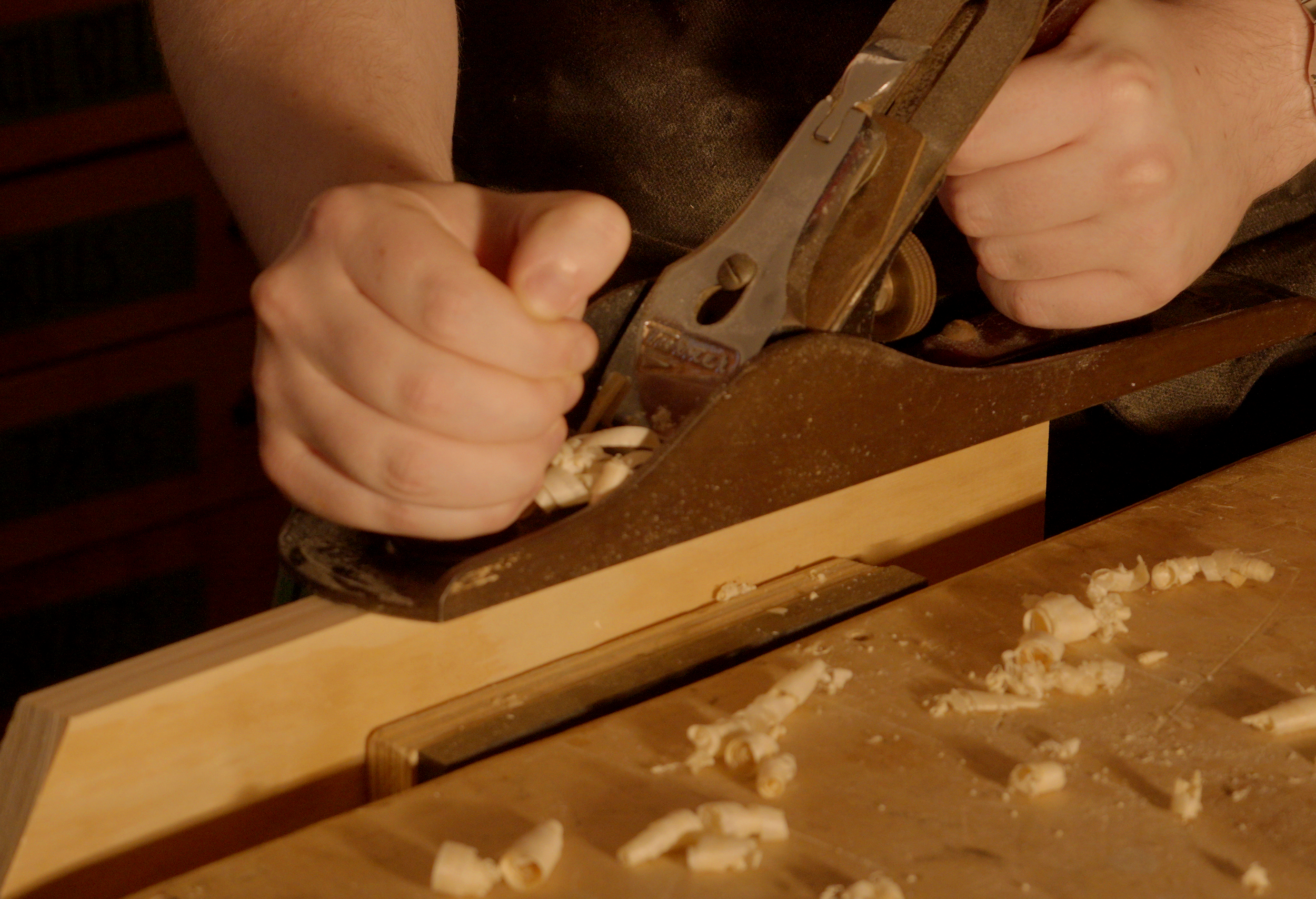 Person planing a piece of wood with a hand planer.