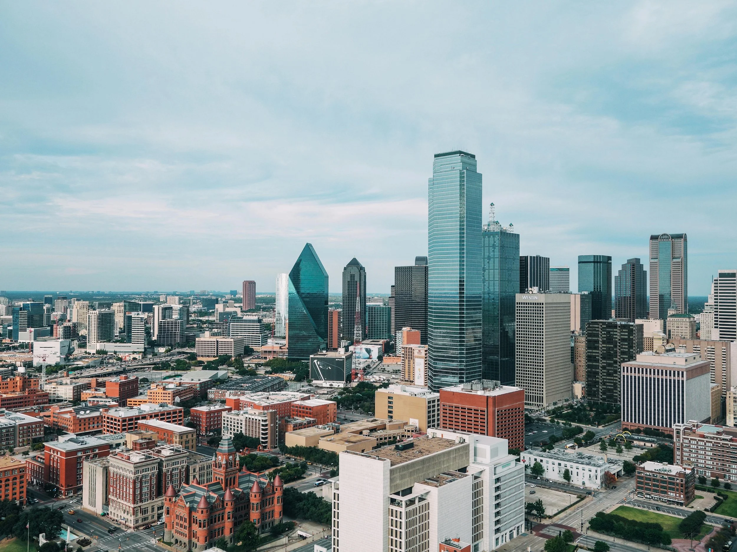 A panoramic view of Dallas, Texas skyline with high-rise buildings against a partly cloudy sky.
