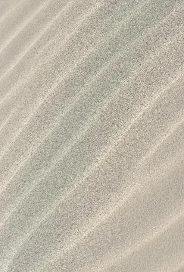 Close-up of white sand dunes with textured, wavy surface patterns.