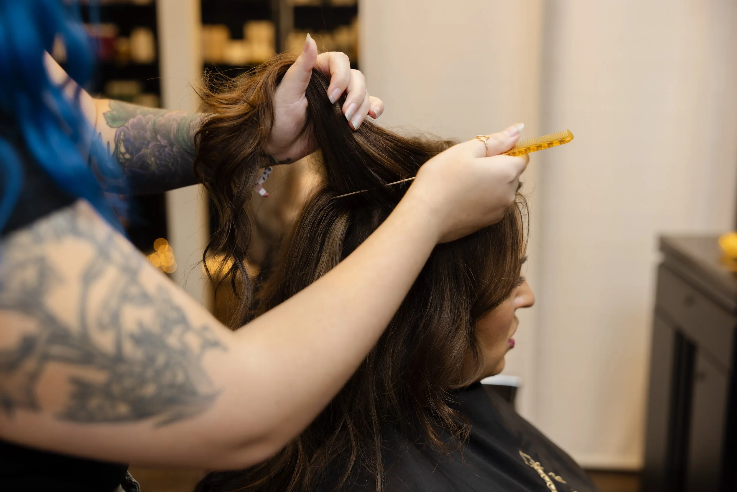 Hairdresser styling a woman's hair with a yellow comb in a salon.