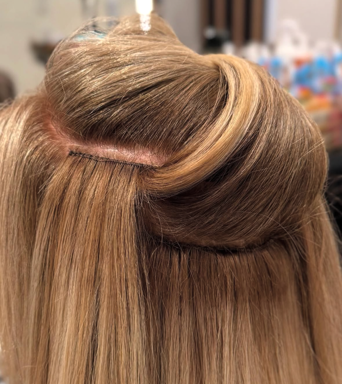 Close-up of a hair extension or wig with blonde and light brown hair, stitched at the top.