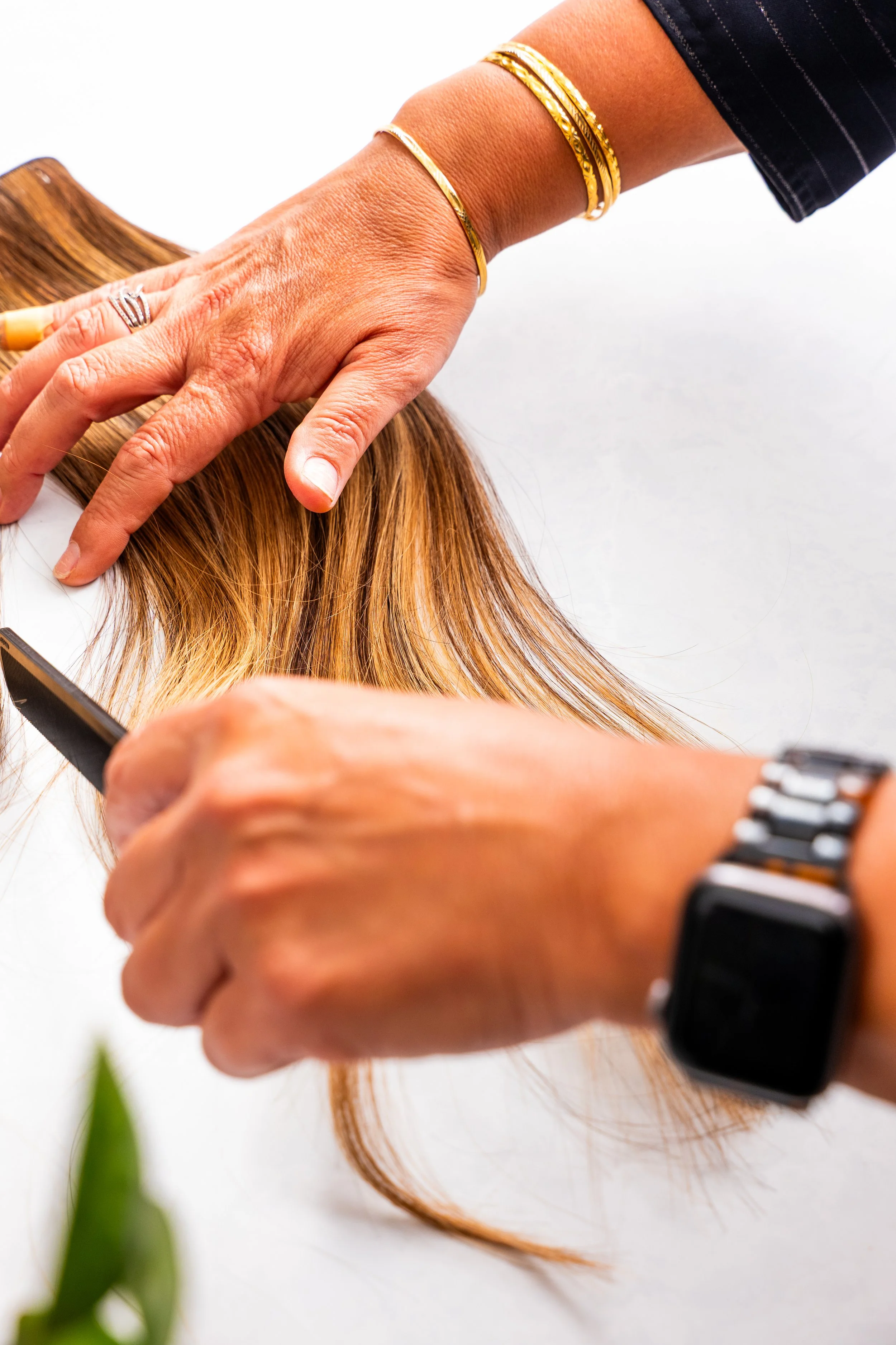 A hairstylist is trimming a woman's long, auburn hair with scissors, with her hand resting on the hair.