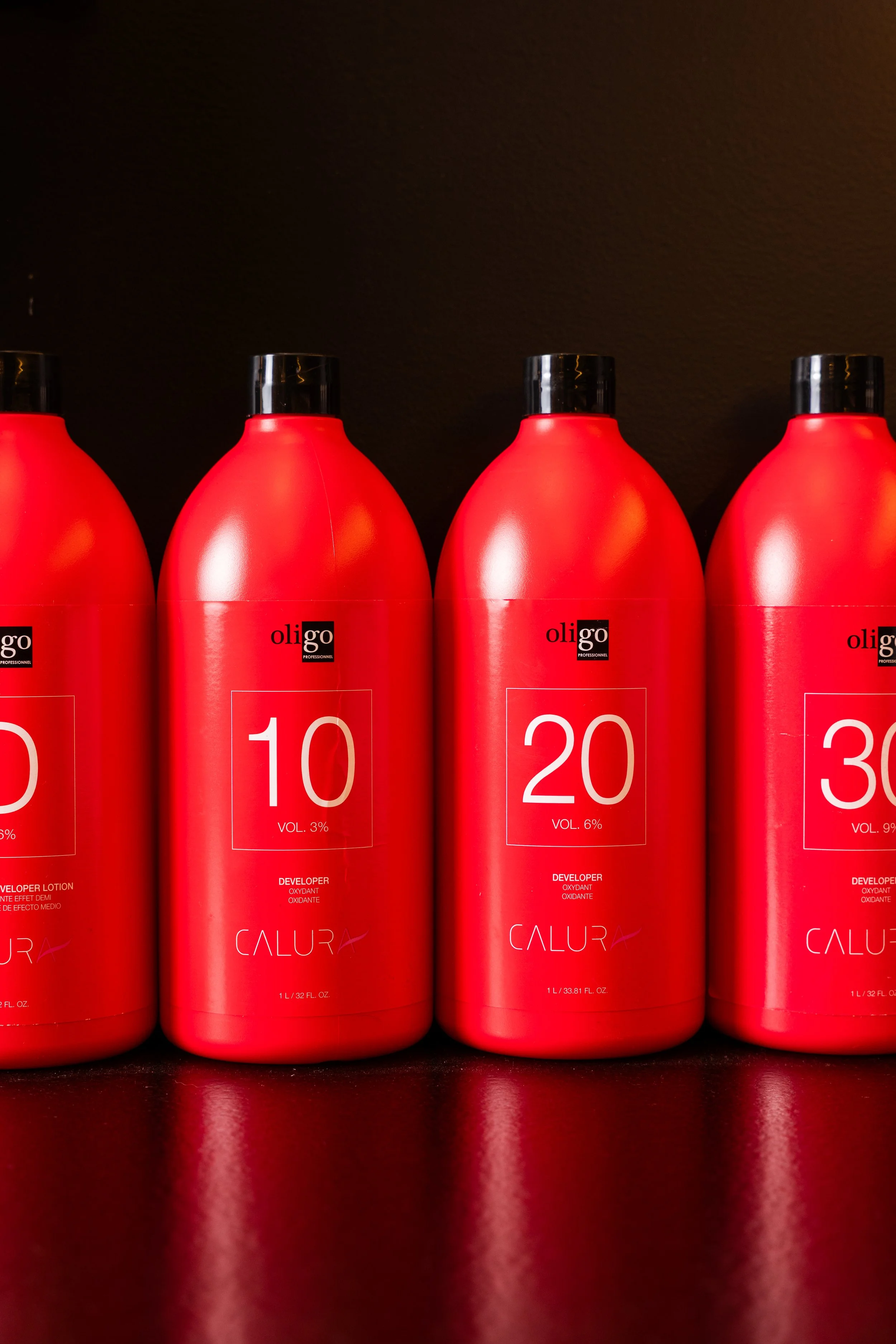 Red bottles of hair developer solution labeled with numbers 10, 20, and 30, placed against a black background.