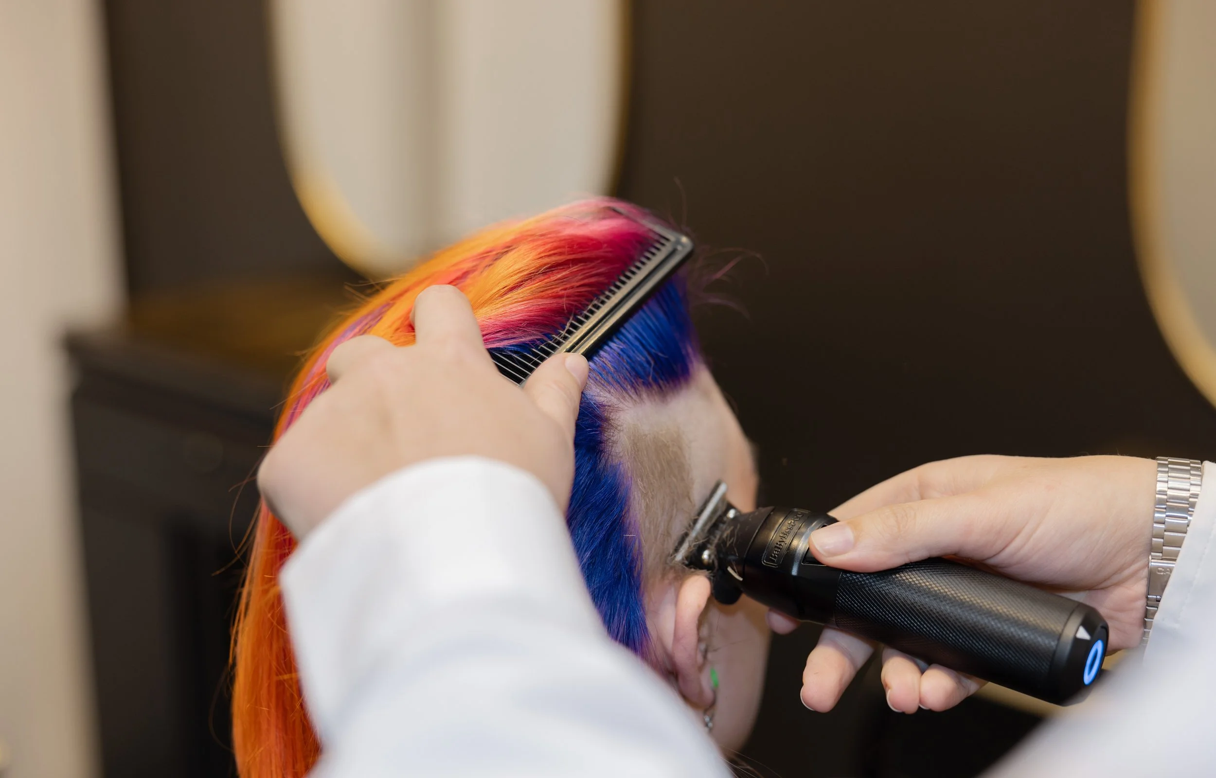 Person getting a haircut with vibrant rainbow-colored hair using clippers and a comb.
