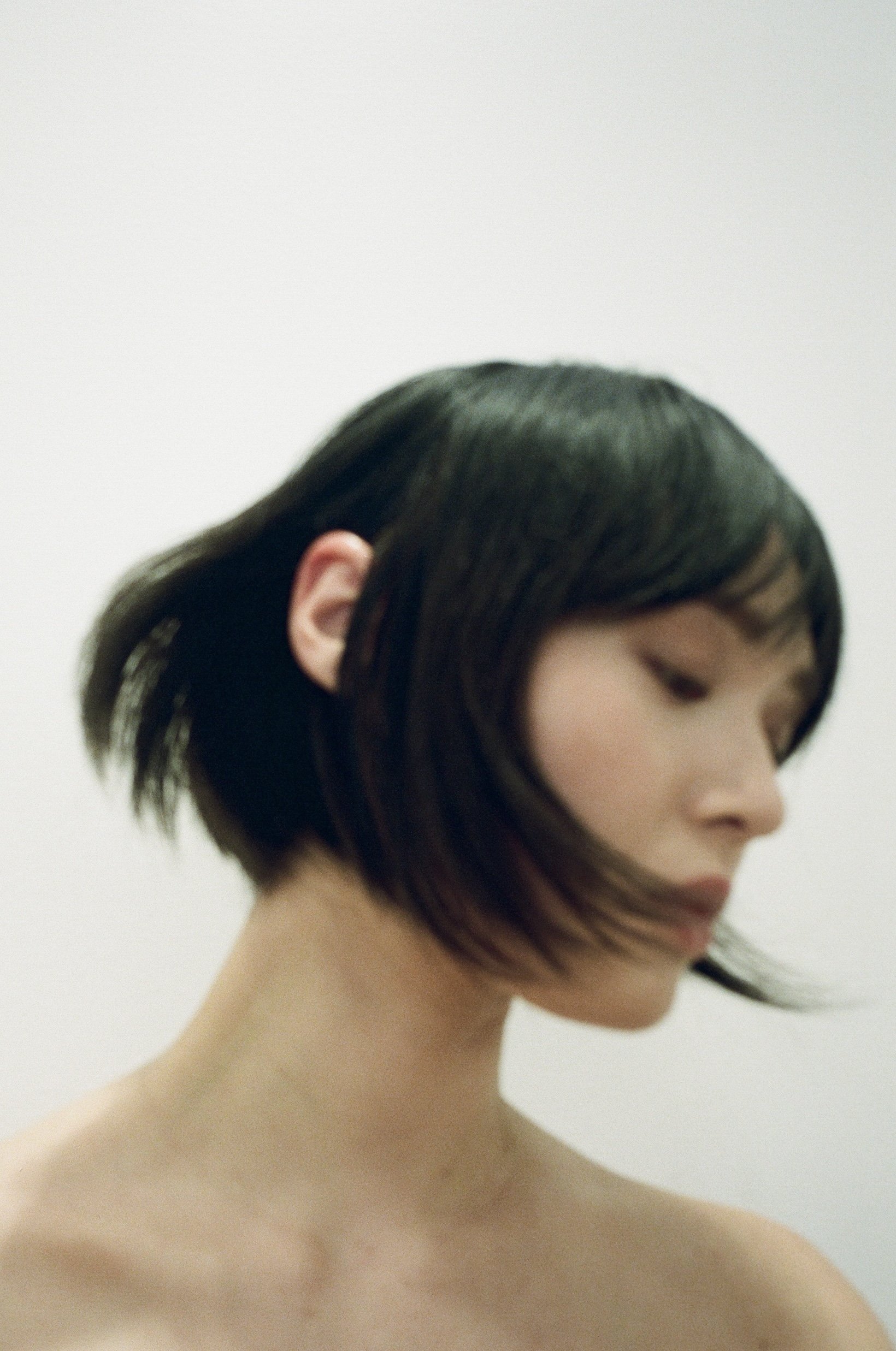 Portrait of a woman with short black hair, looking down, against a plain background.