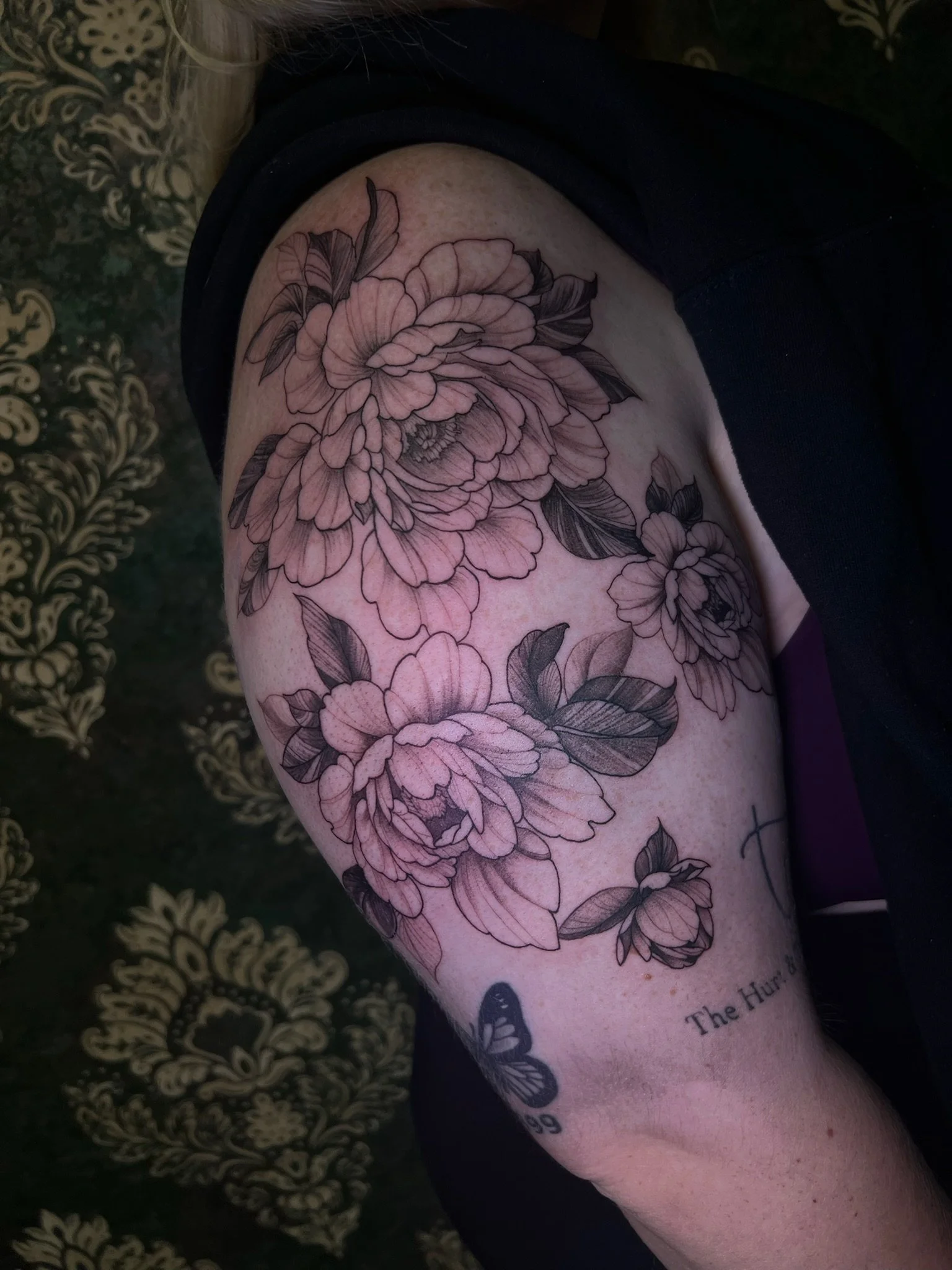 Black and gray floral tattoo with roses and leaves on a person's upper arm.