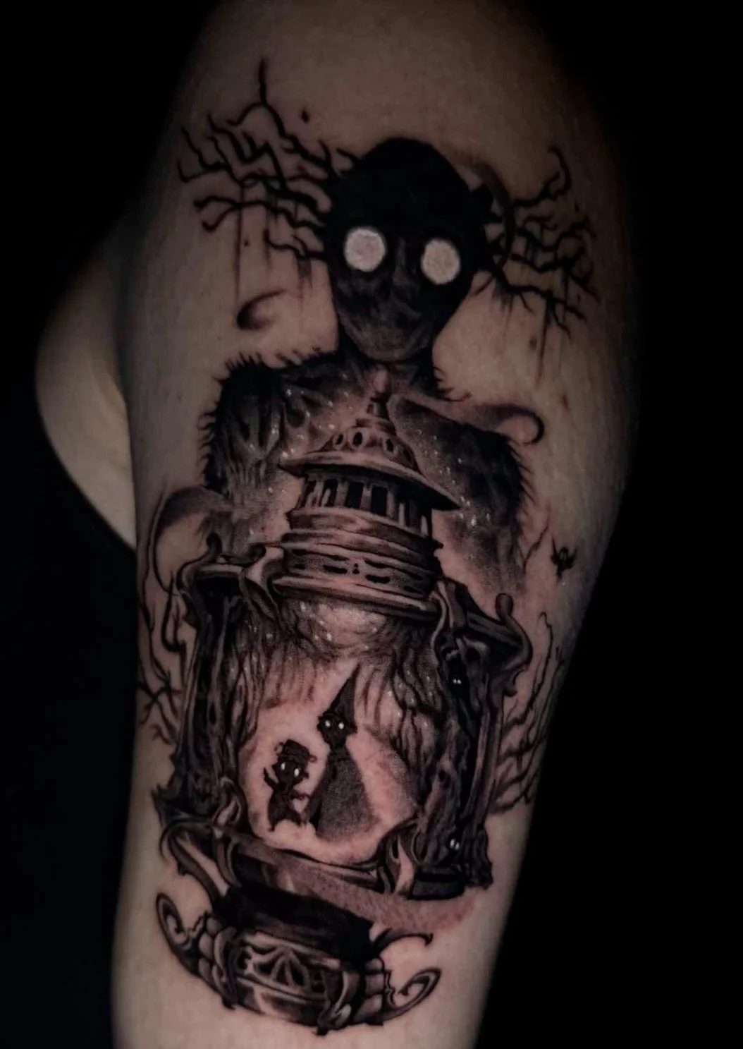 Tattoo of a creepy doll with glowing eyes and black veins on the forehead, a pickaxe, and a small silhouette of two people inside an hourglass on a person's arm.