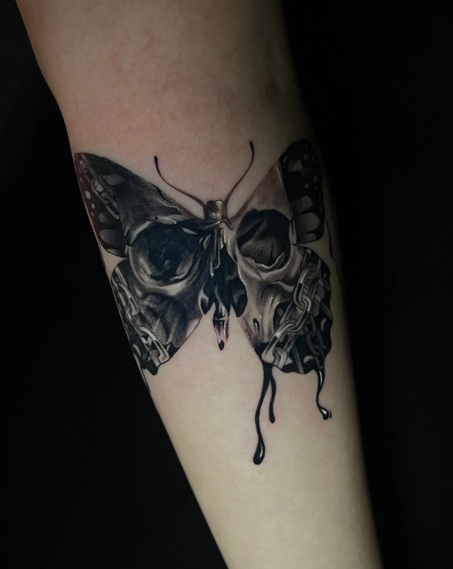 Black and gray tattoo of a butterfly with broken chain design on person's arm.