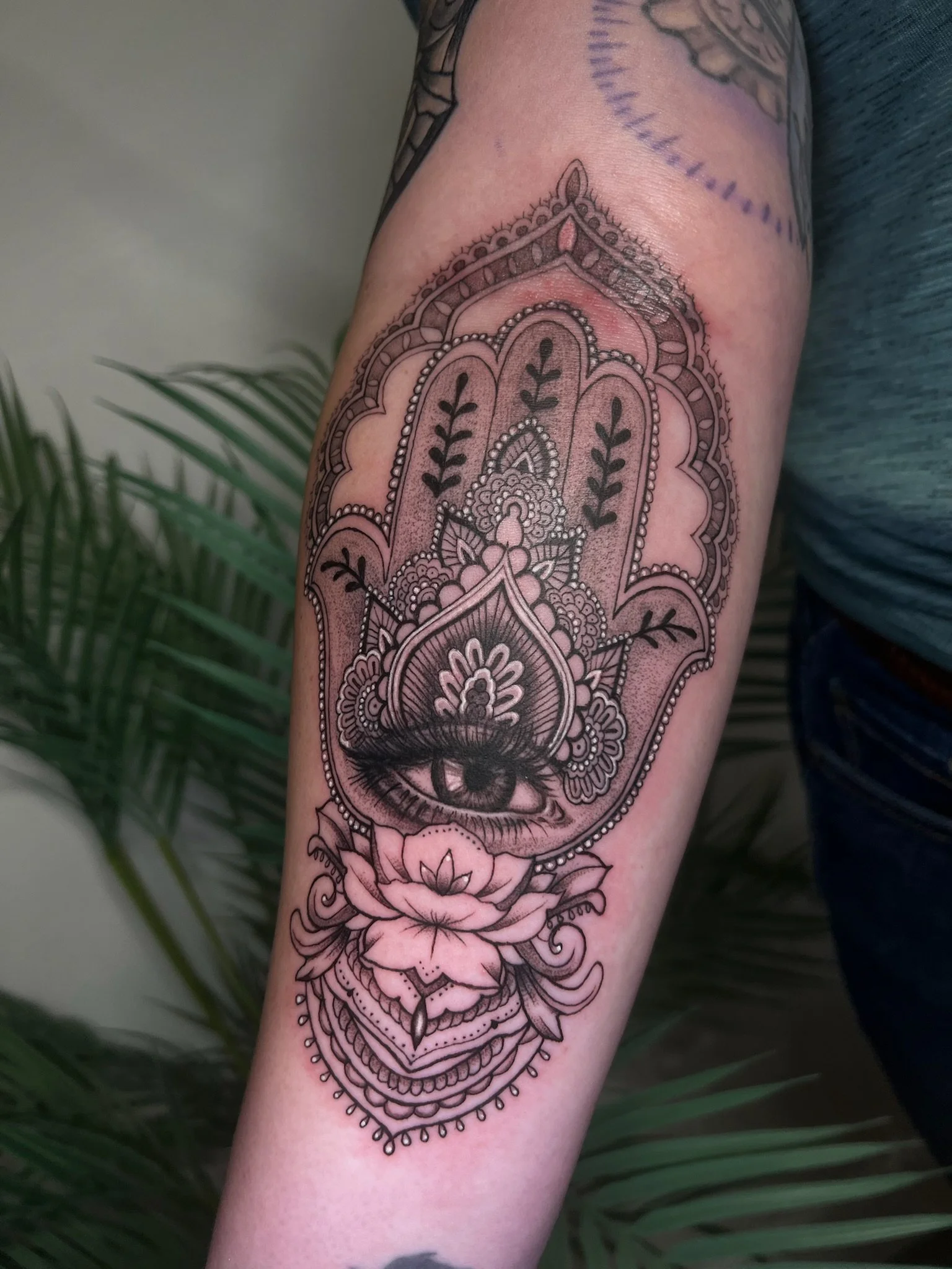 Tattoo of an eye with floral and ornamental patterns around it on a person's forearm.
