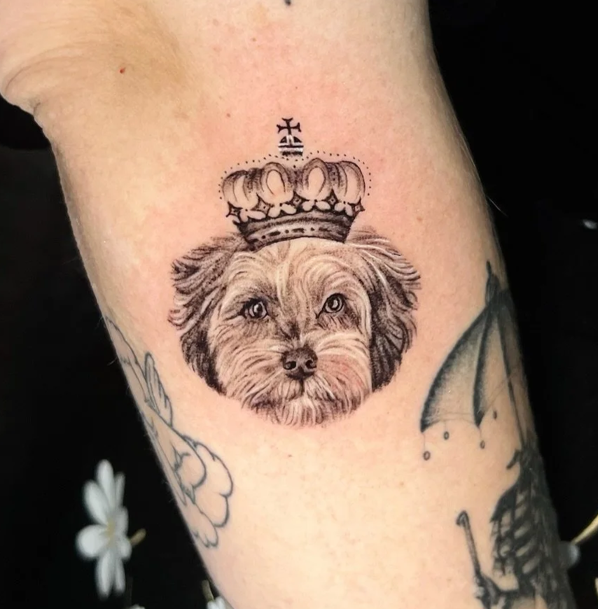 Tattoo of a dog's face wearing a crown.