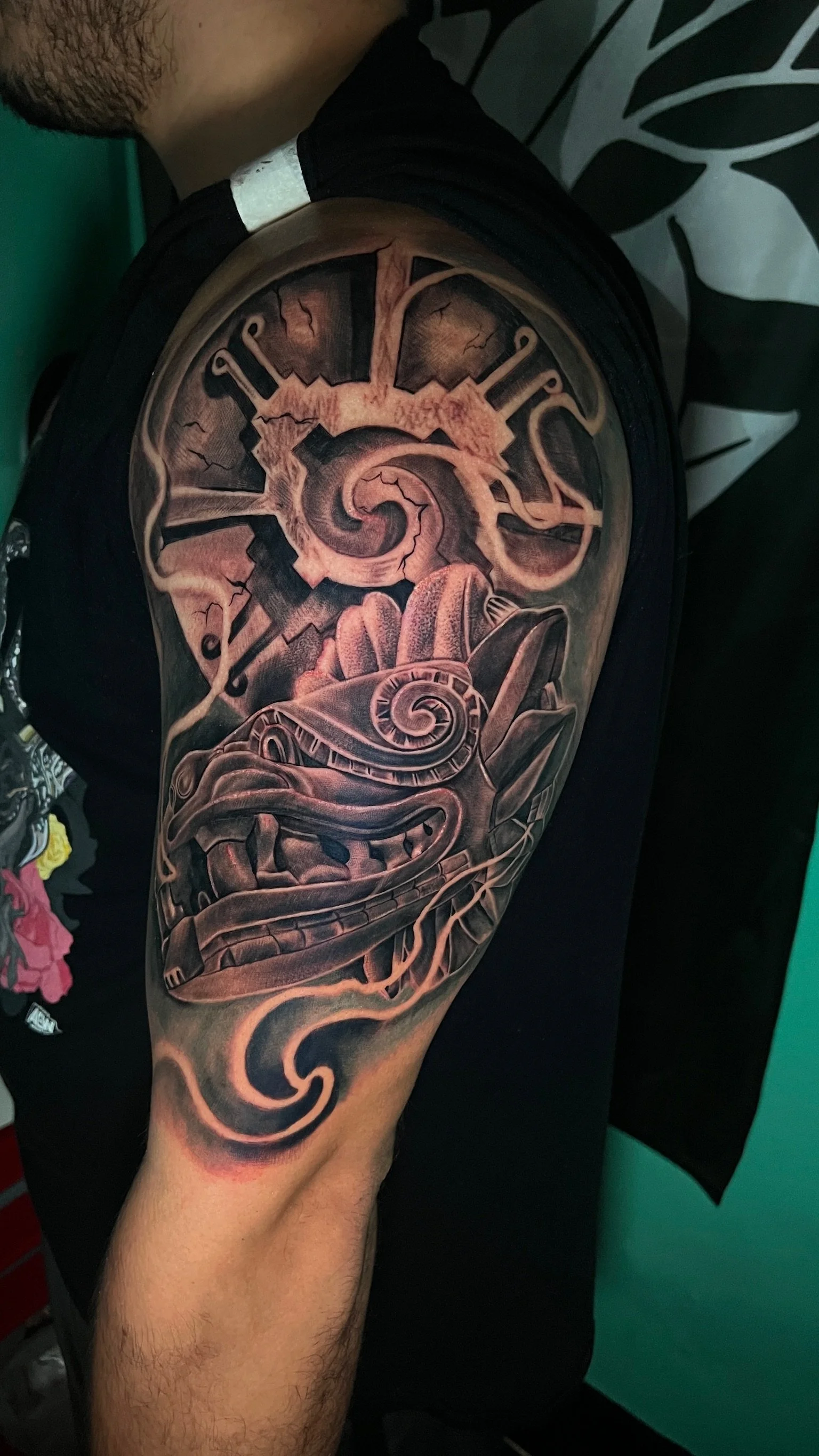 A black and gray robotic dragon tattoo on a person's shoulder and upper arm, featuring intricate details and shading.