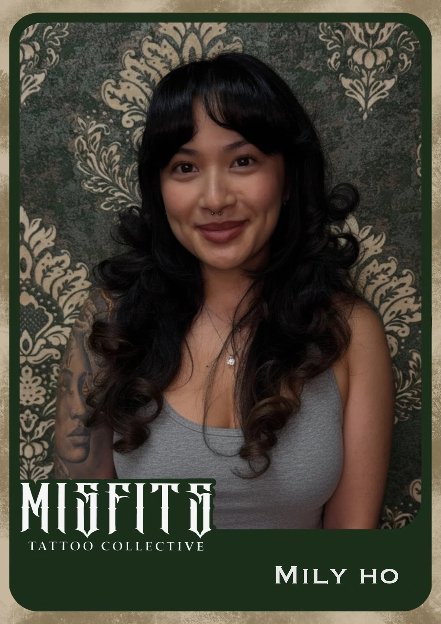 A young woman with dark, curly hair and a septum piercing, smiling at the camera. She is wearing a gray tank top and a necklace. The background is a patterned wallpaper. The image appears to be part of a tattoo collectable card with the text 'Misutto Tattoo Collective' and the name 'Mily Ho' at the bottom.