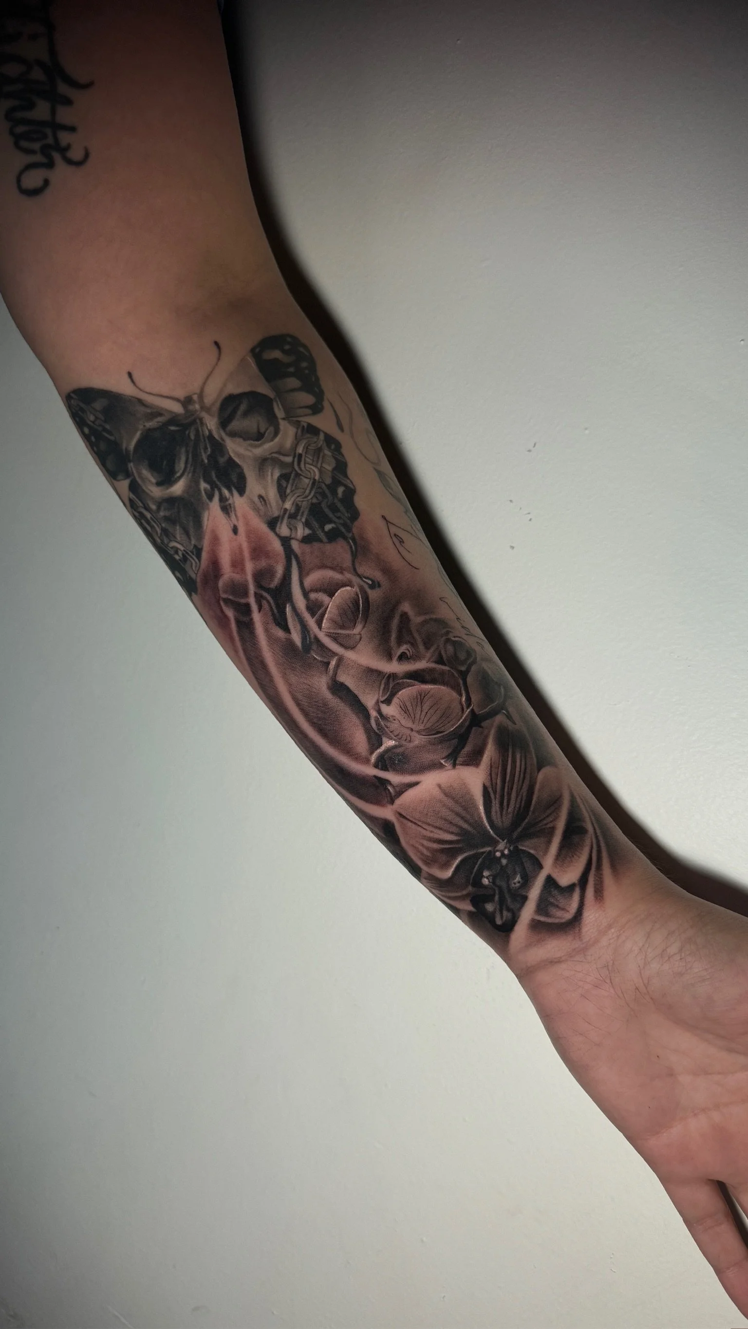 Tattoo of a butterfly, skull, and flowers on a person's forearm.