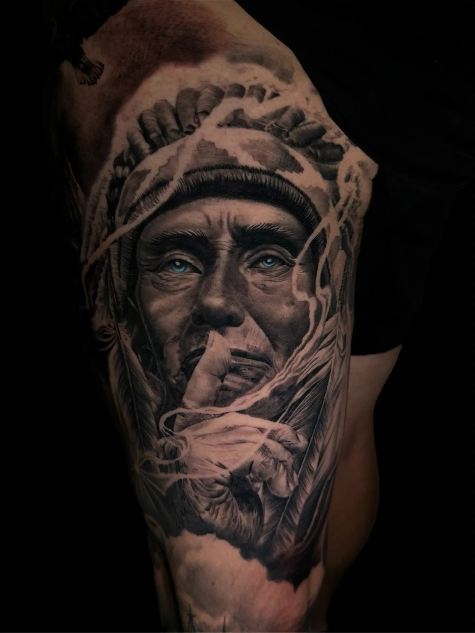 Black and gray tattoo of a woman with blue eyes, wearing a headscarf, holding a finger to her lips, with detailed shading and realistic style.