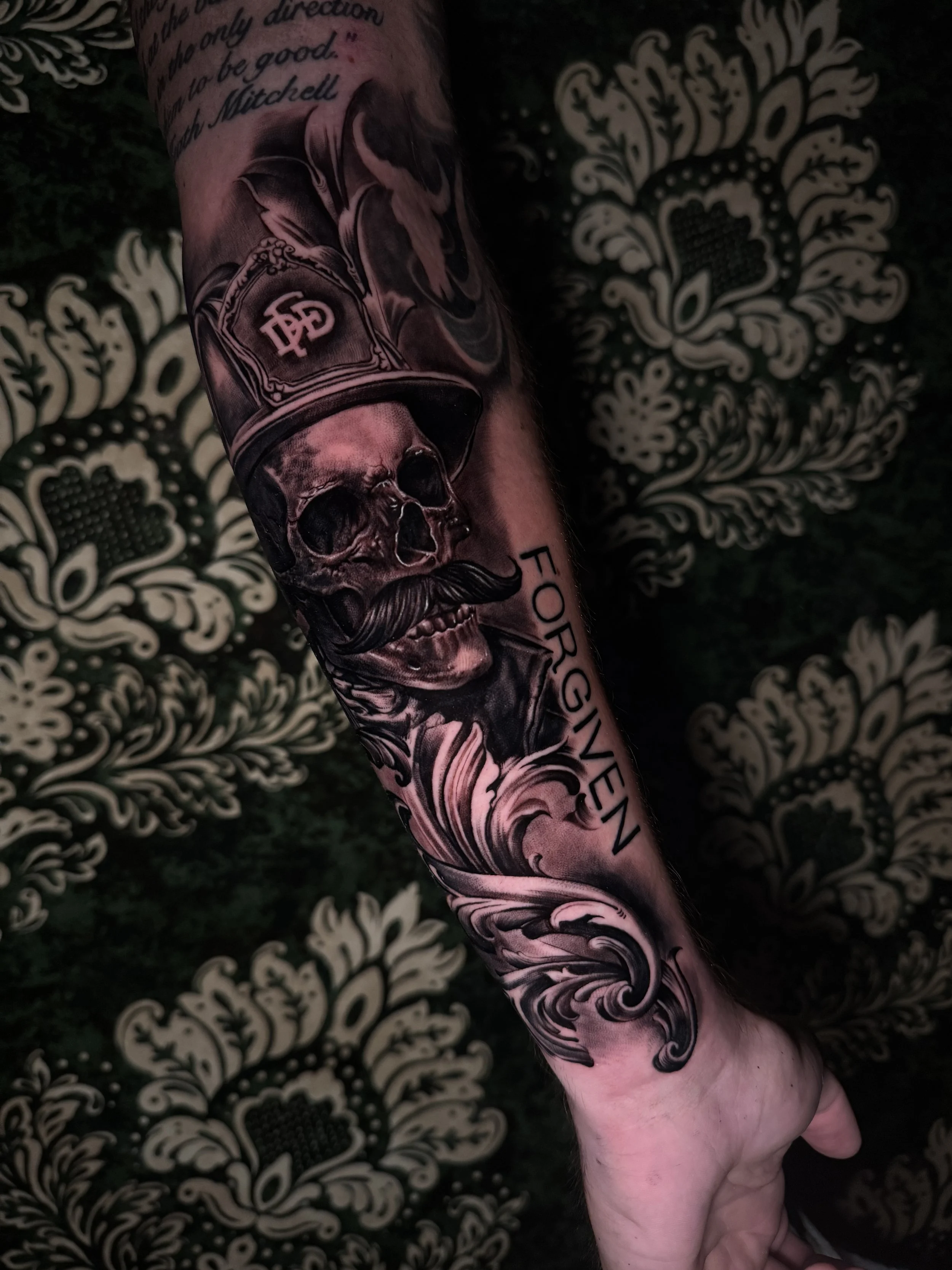 Tattoo on forearm featuring a skull wearing a firefighter helmet with smoke, surrounded by decorative swirling patterns and the words 'FOR GIVEN'.