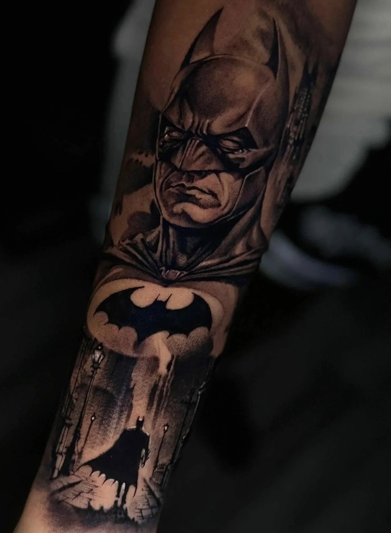 Tattoo of Batman with a dark cityscape background and Bat-symbol on the arm.