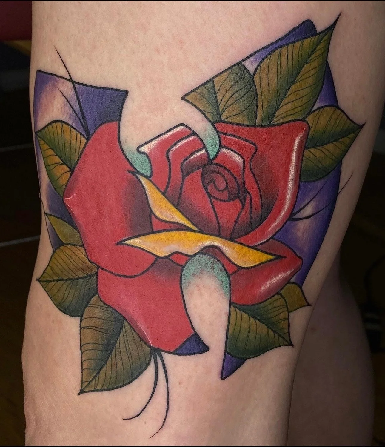 Colorful tattoo of a red rose with green leaves on skin.
