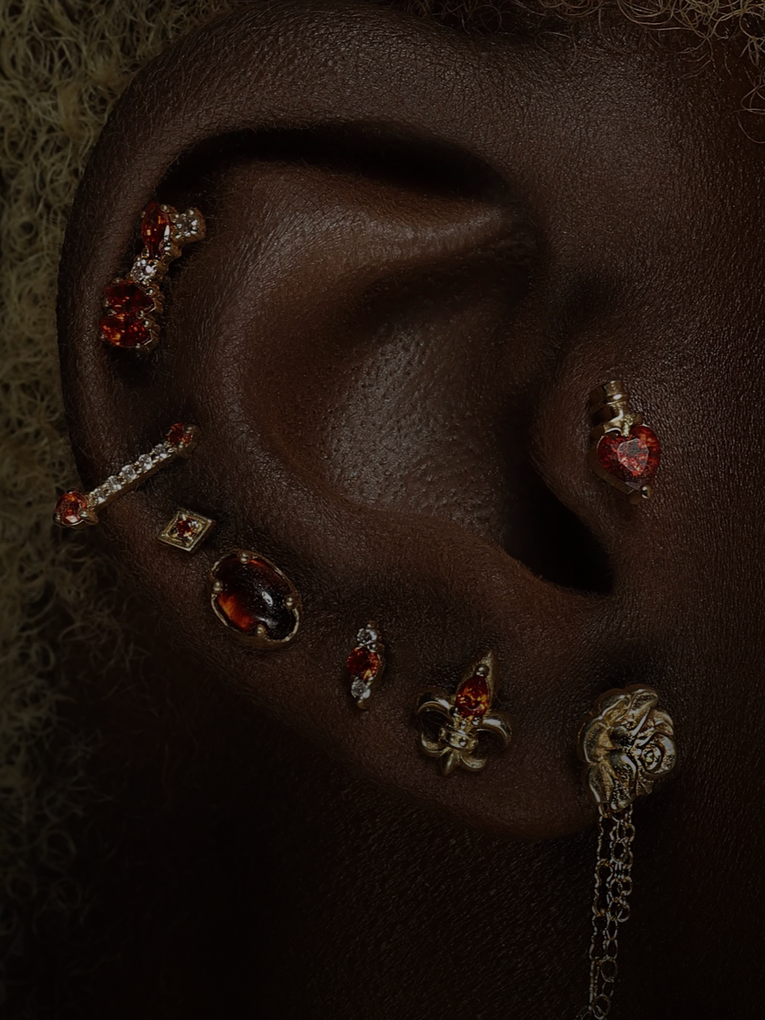 Close-up of a person's ear decorated with multiple earrings, including a heart-shaped gem, a skull, and various other ornate earrings.