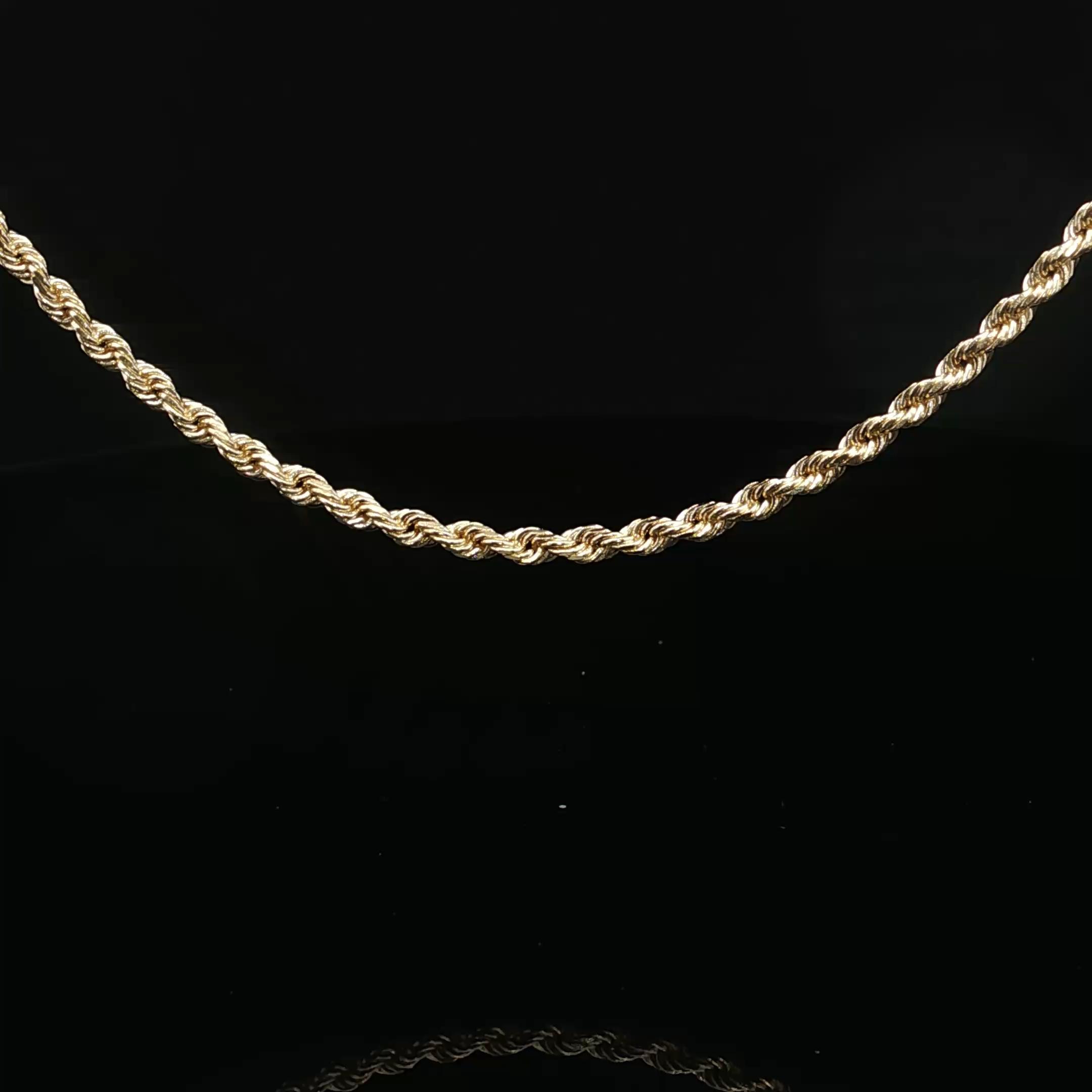 Close-up of a twisted gold chain necklace against a black background.