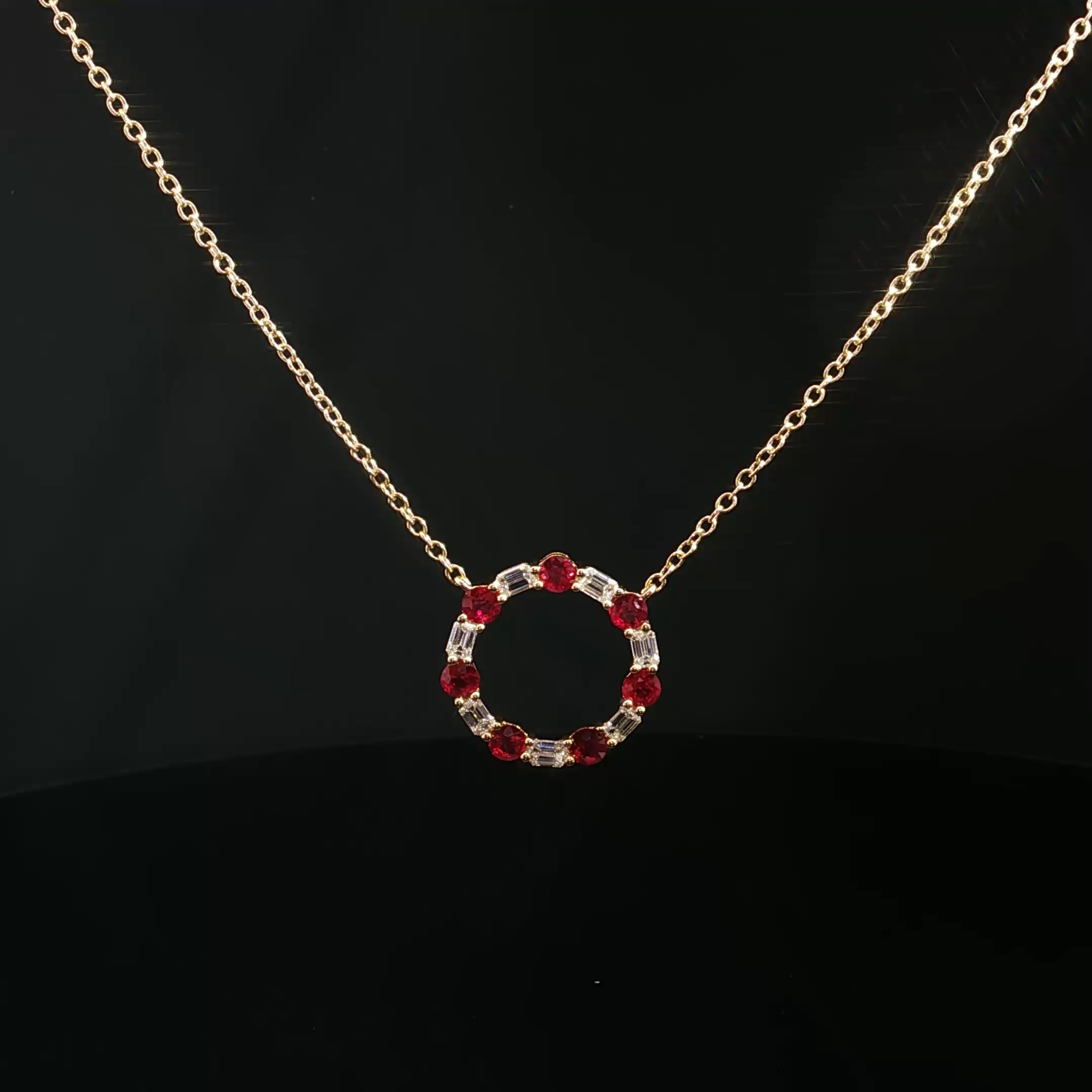 Gold chain necklace with a pendant featuring red gemstones and clear rectangular gemstones on a black background.