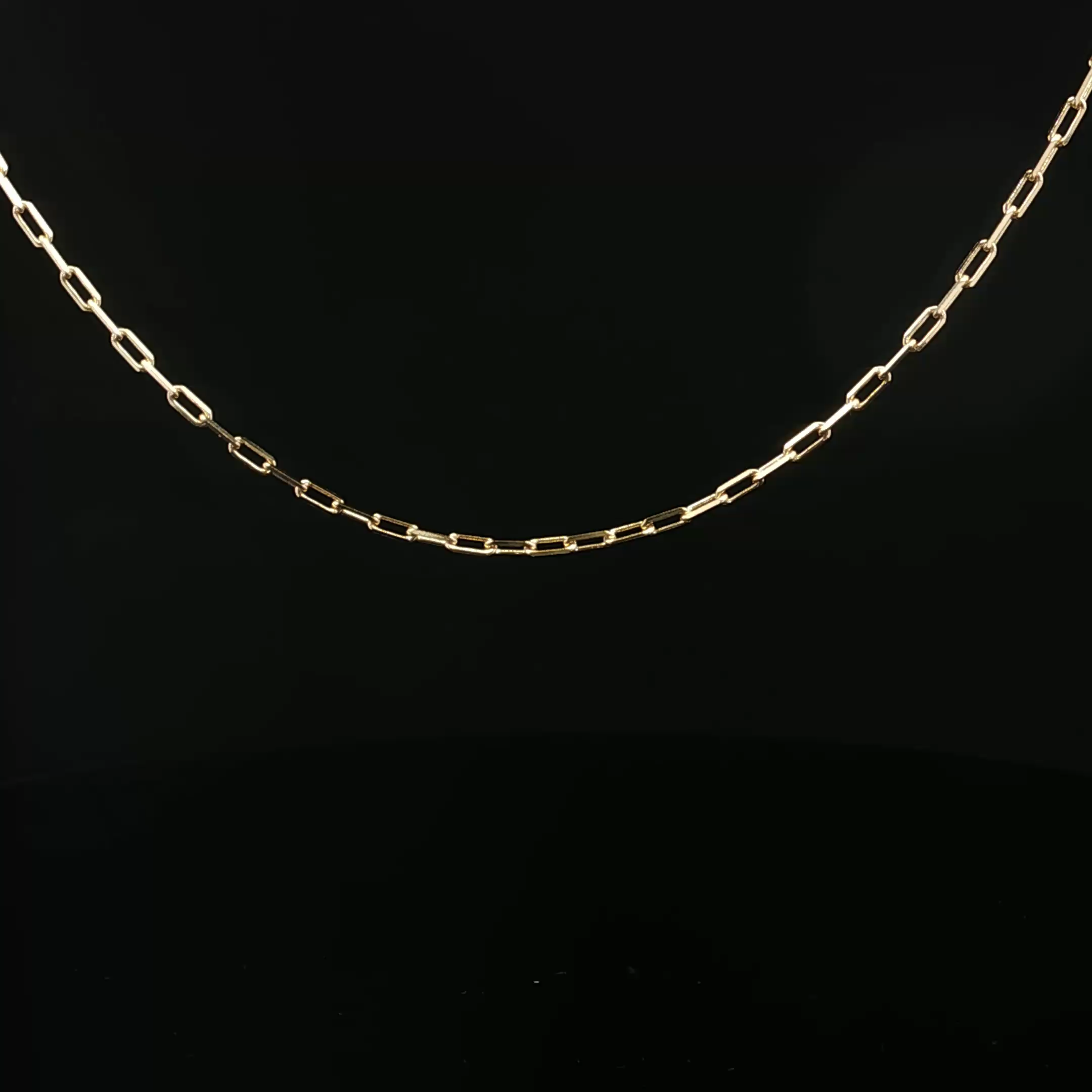 A gold chain necklace with rectangular links, displayed against a black background.