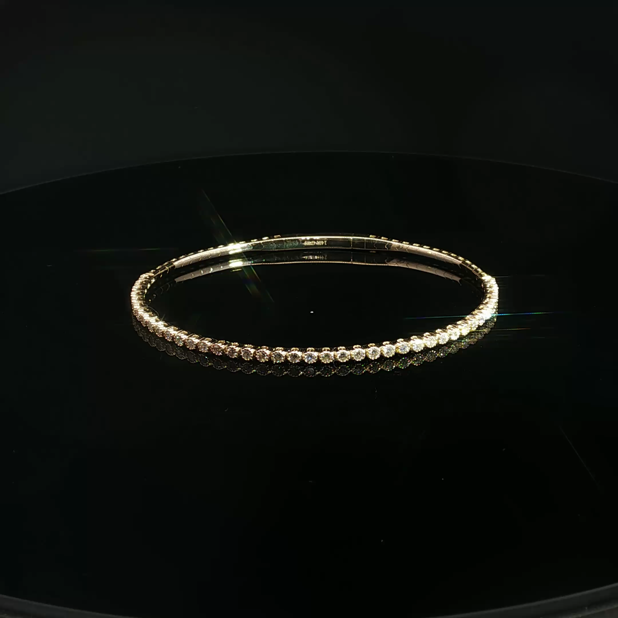 A close-up photo of a circular diamond bracelet with a black background, illuminated by yellowish light.