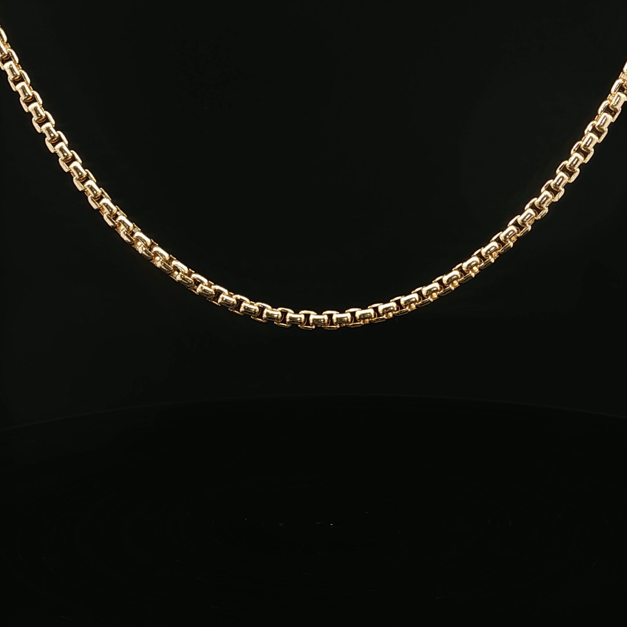 Close-up of a gold chain necklace against a black background.