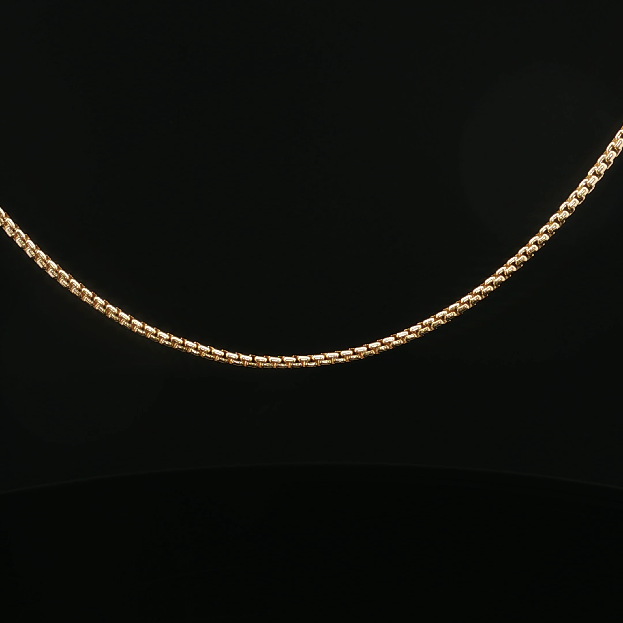 Close-up of two gold chains with intricate links on a black background.