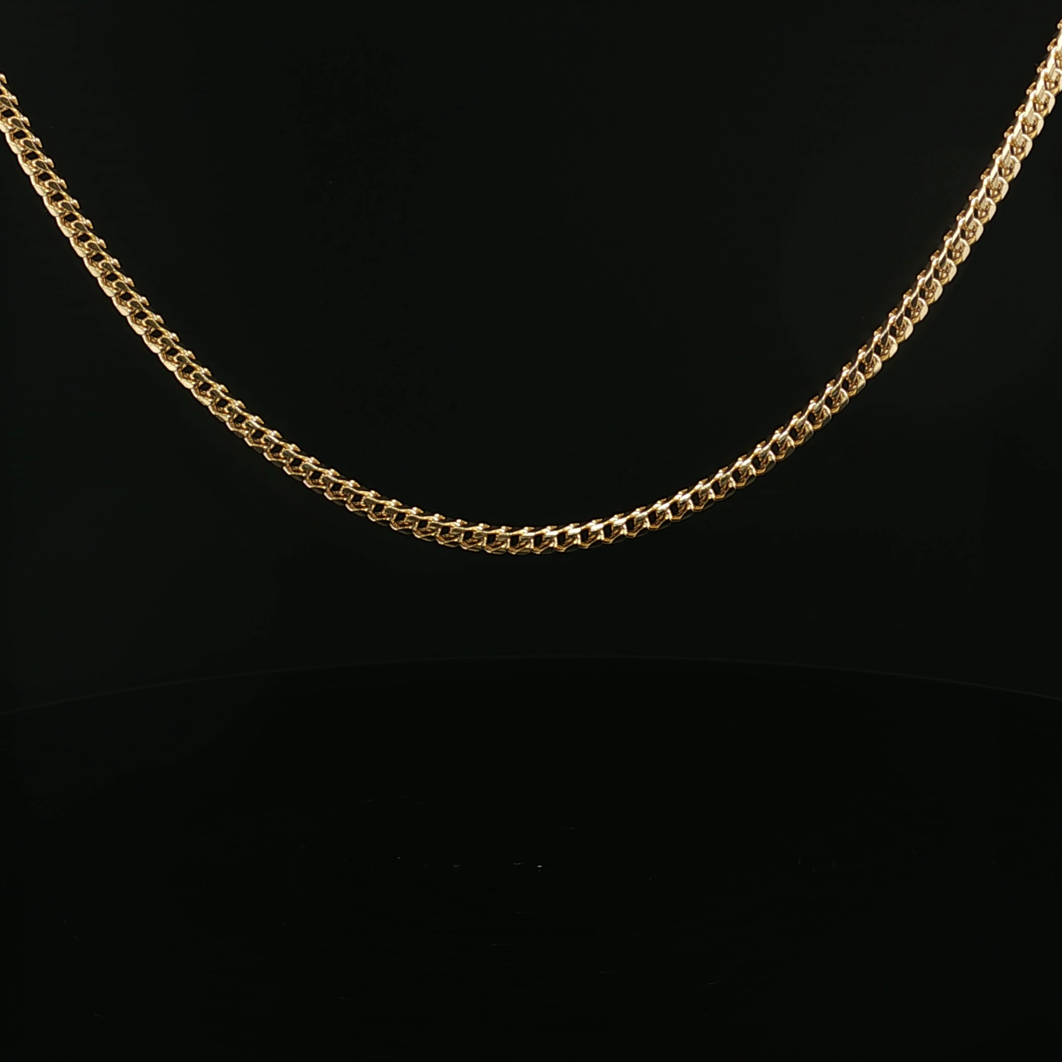 Close-up of a gold chain necklace on a black background.