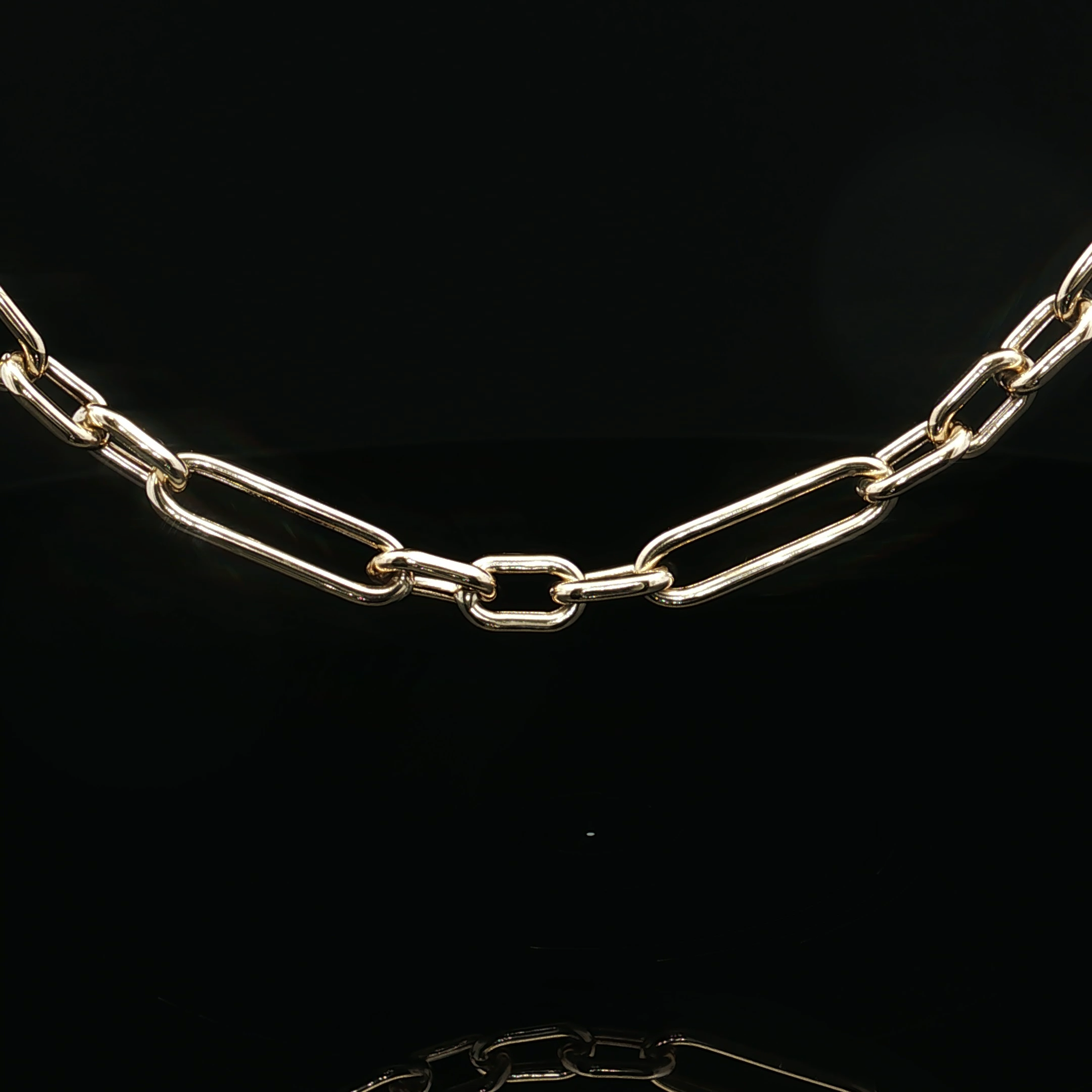 Close-up of a white gold paperclip like chain necklace against a black background.